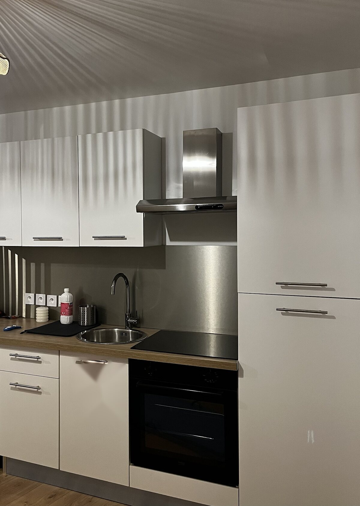 Cuisine blanche avec crédence inox, hotte et four encastré